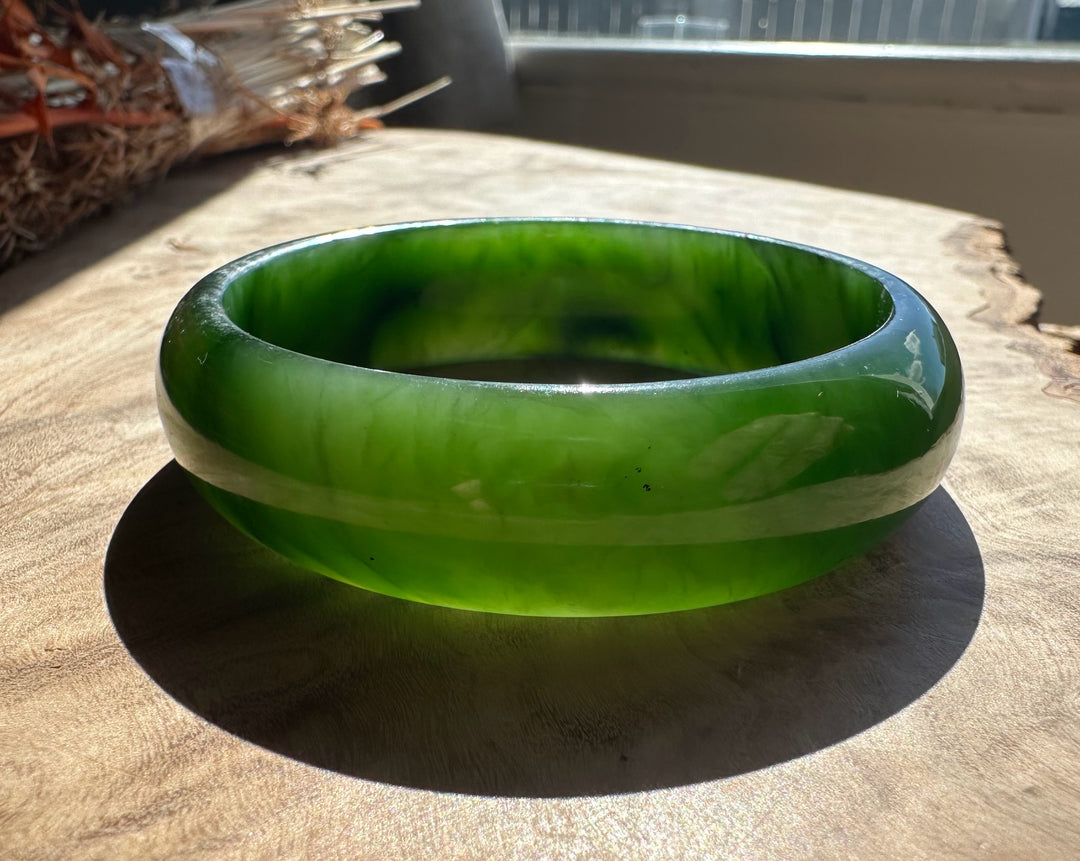 Jade bangle in vivid green with lighter banding and a glossy finish resting on a wooden surface