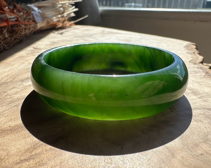 Jade bangle in vivid green with lighter banding and a glossy finish resting on a wooden surface