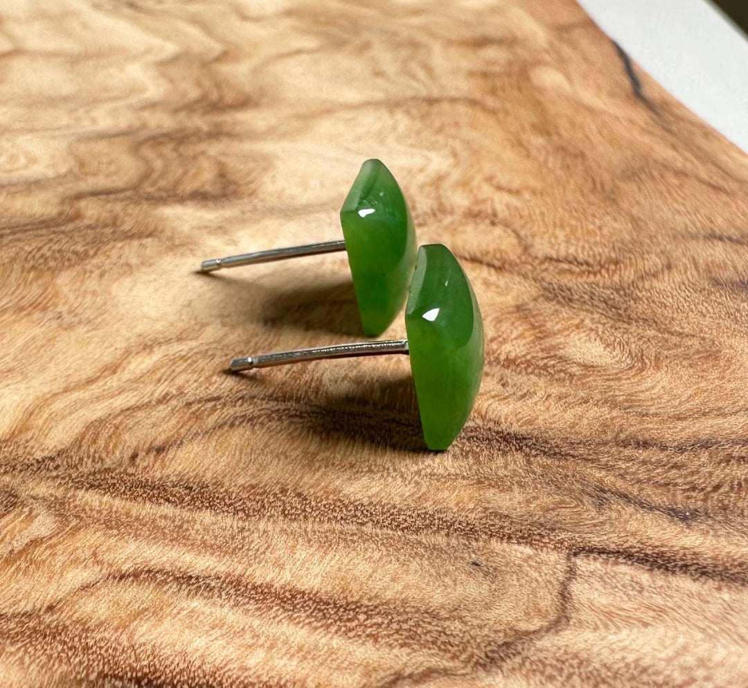 Angle shot of green jade square stud earrings with silver posts on a wood grain surface