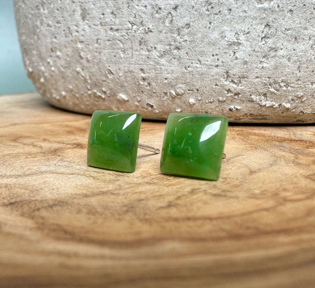 Pair of green jade square stud earrings with silver posts on a wooden surface