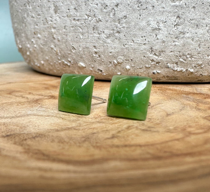 Pair of green jade square stud earrings with silver posts on a wooden surface
