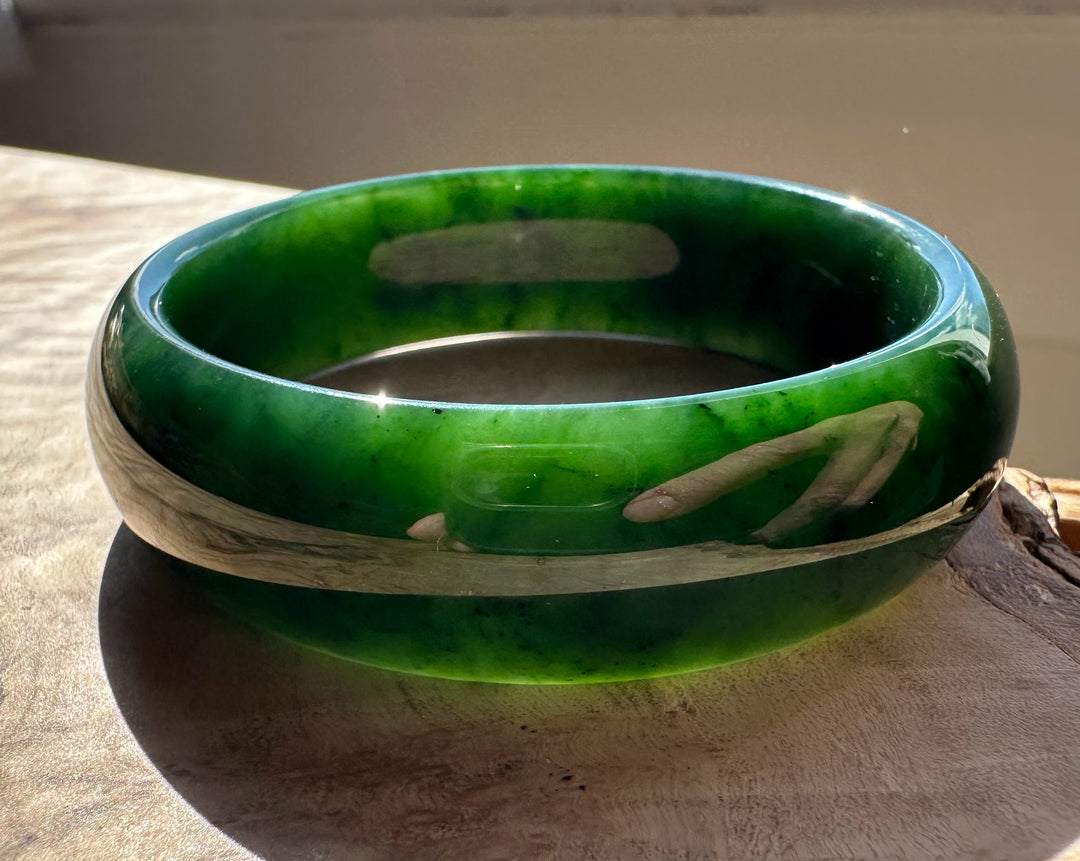 Canadian jade bangle in bright green with pale white banding resting on a wooden surface.