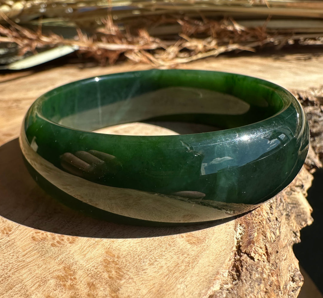 Canadian Jade Bangle 54 x 17mm glossy green band with reflective surface on wood.