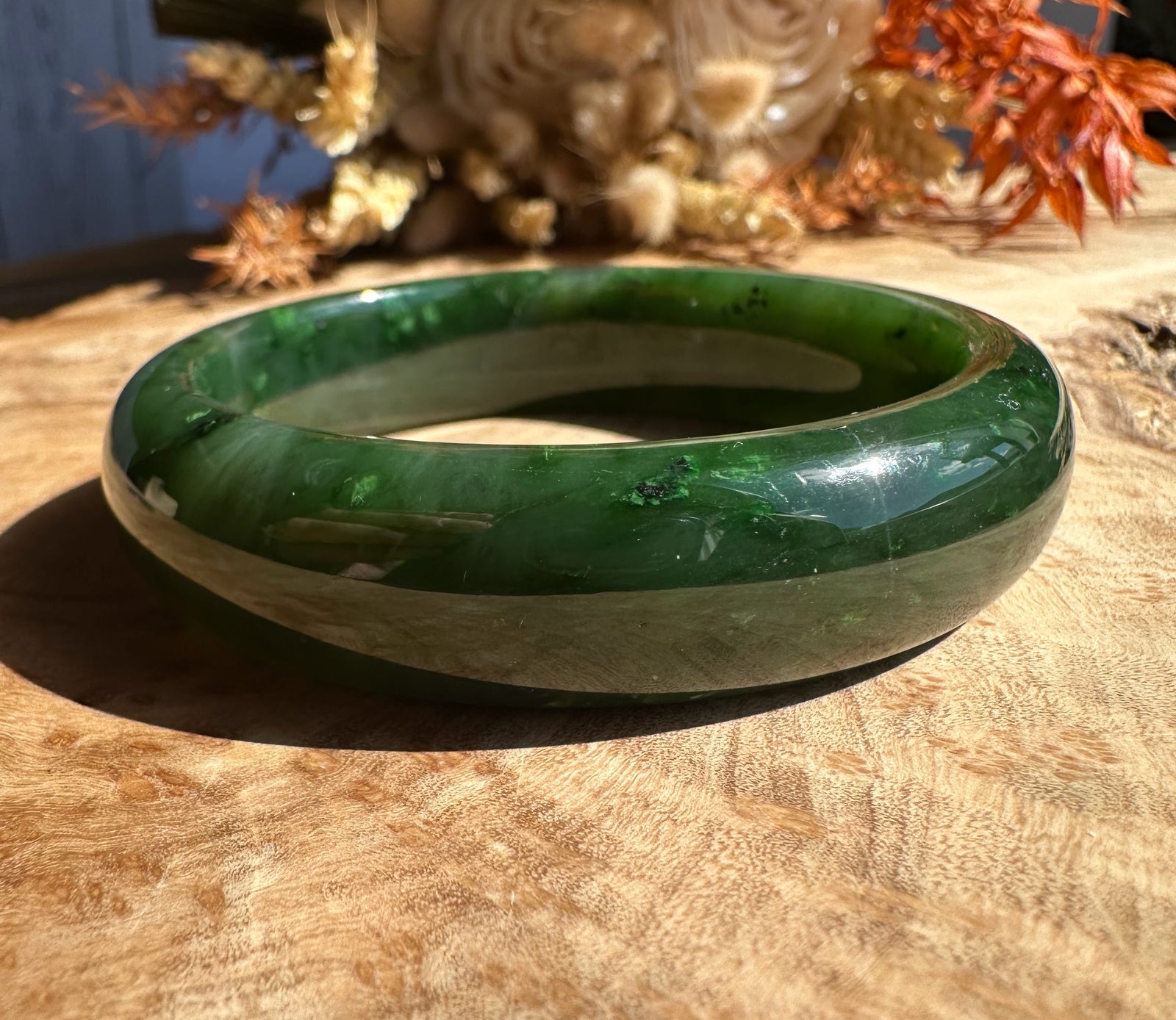 Canadian jade bangle 56 x 15.5mm in two tone green with light banding on a wooden surface