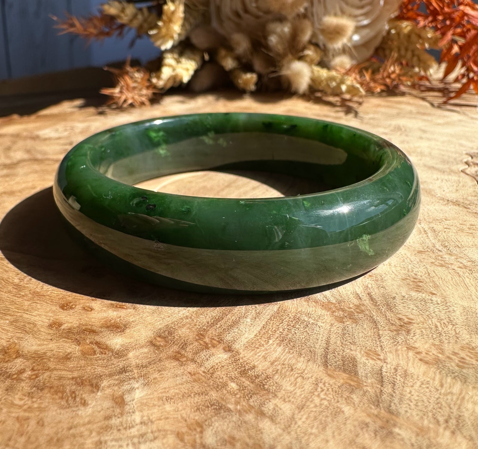 Close up of Canadian jade bangle showing rich green exterior and pale inner layer on wood surface