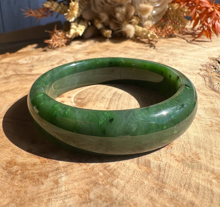 Canadian Jade Bangle 56 x 15.5mm in polished green jade on a wooden surface viewed from a slight angle