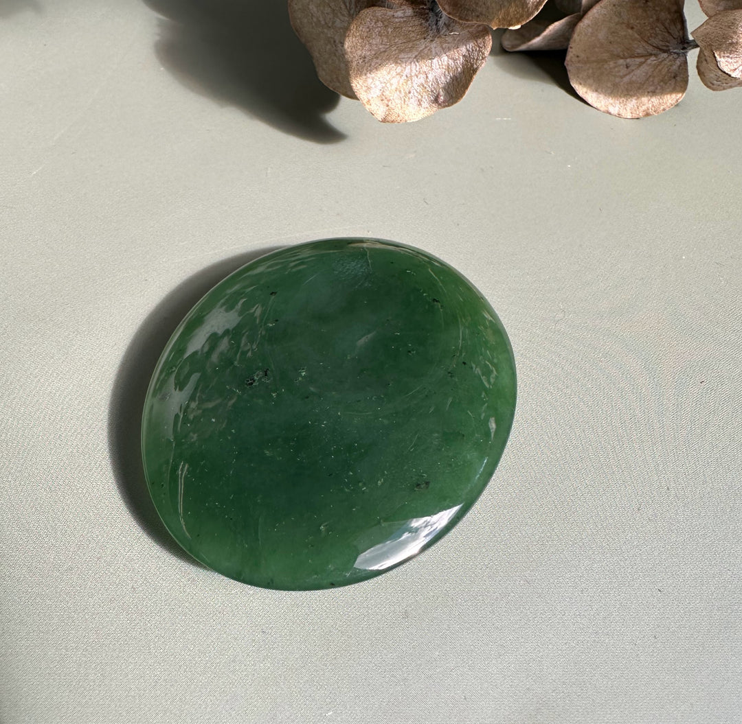Polished round Canadian jade worry stone in deep green with subtle white marbling on a neutral surface