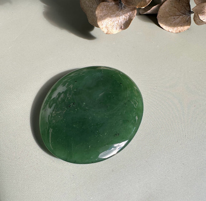 Polished round Canadian jade worry stone in deep green with subtle white marbling on a neutral surface