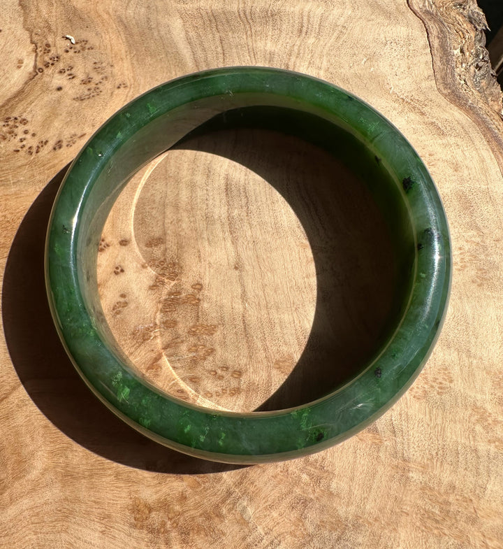 Top-down view of Canadian Jade Bangle 56 x 15.5mm resting on a wooden surface, green jade inner circle visible
