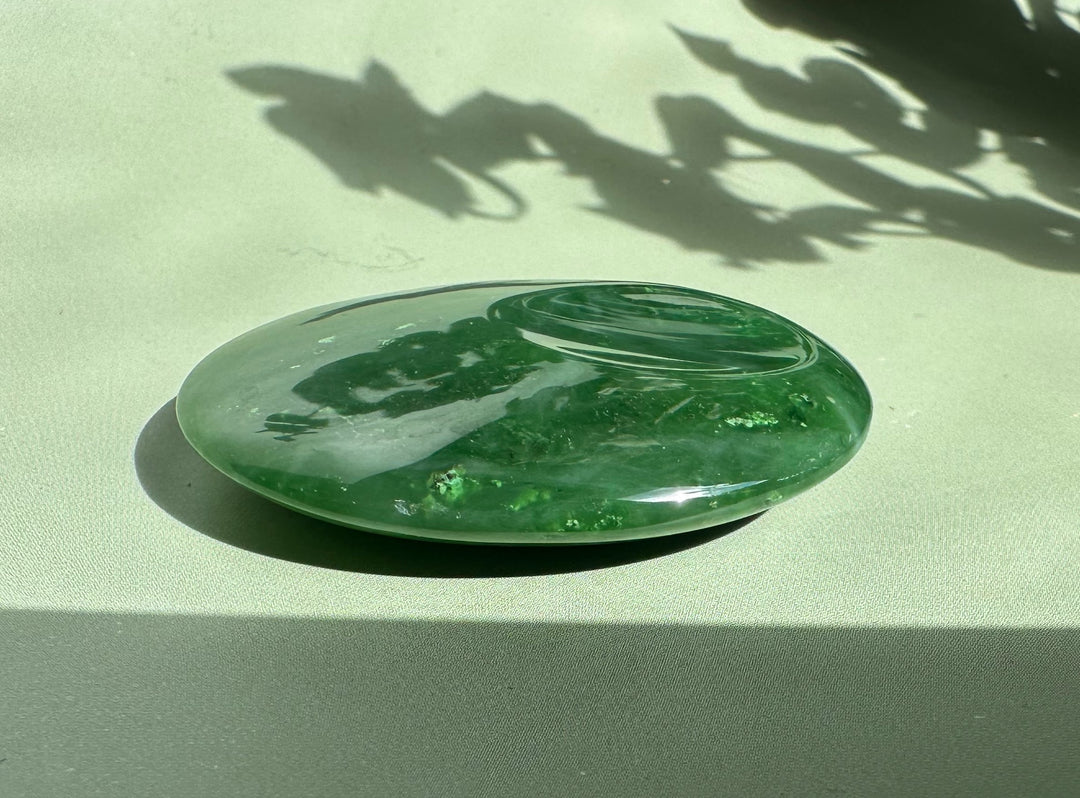 Canadian jade worry stone glossy green oval angled on a pale surface with reflections