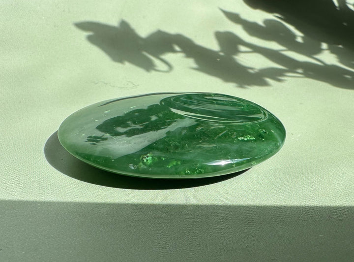 Canadian jade worry stone glossy green oval angled on a pale surface with reflections