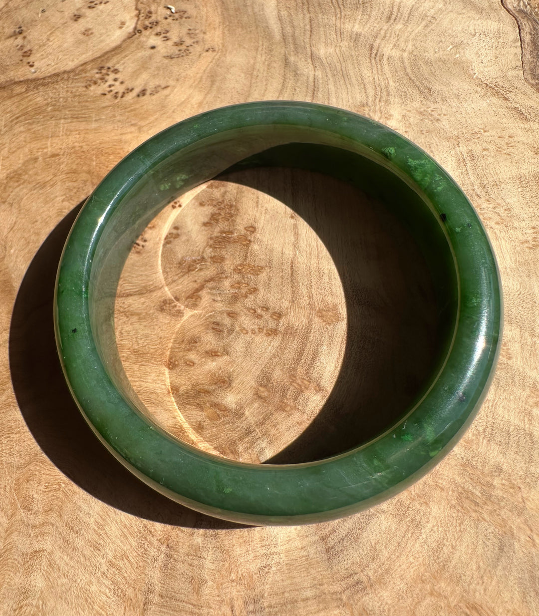 Canadian Jade Bangle 56 x 15.5mm in rich green resting on a wooden surface