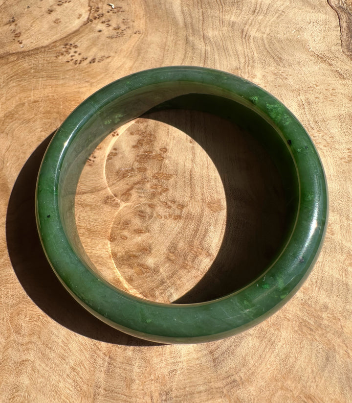 Canadian Jade Bangle 56 x 15.5mm in rich green resting on a wooden surface