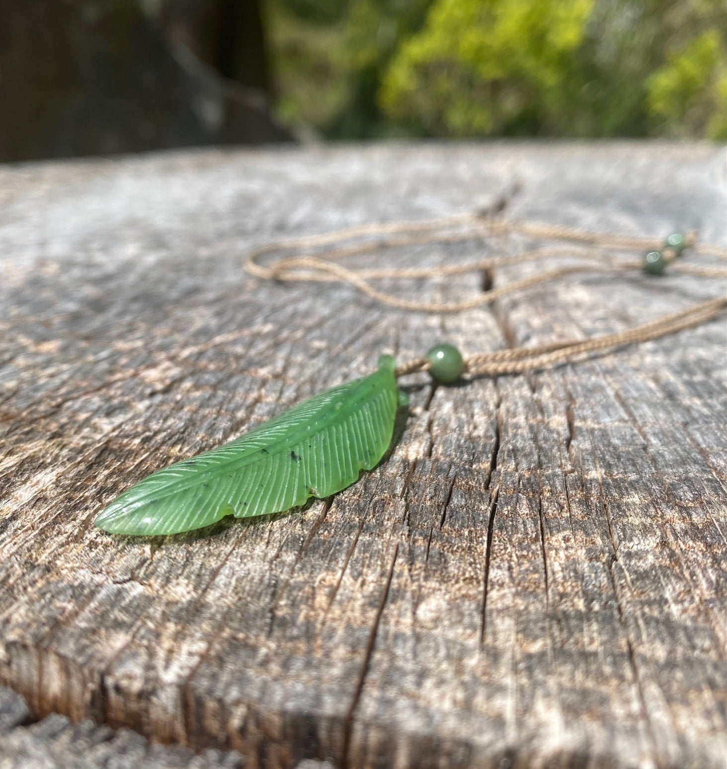 Close up of green leaf jade pendant on a tan cord with a round green bead resting on weathered wood