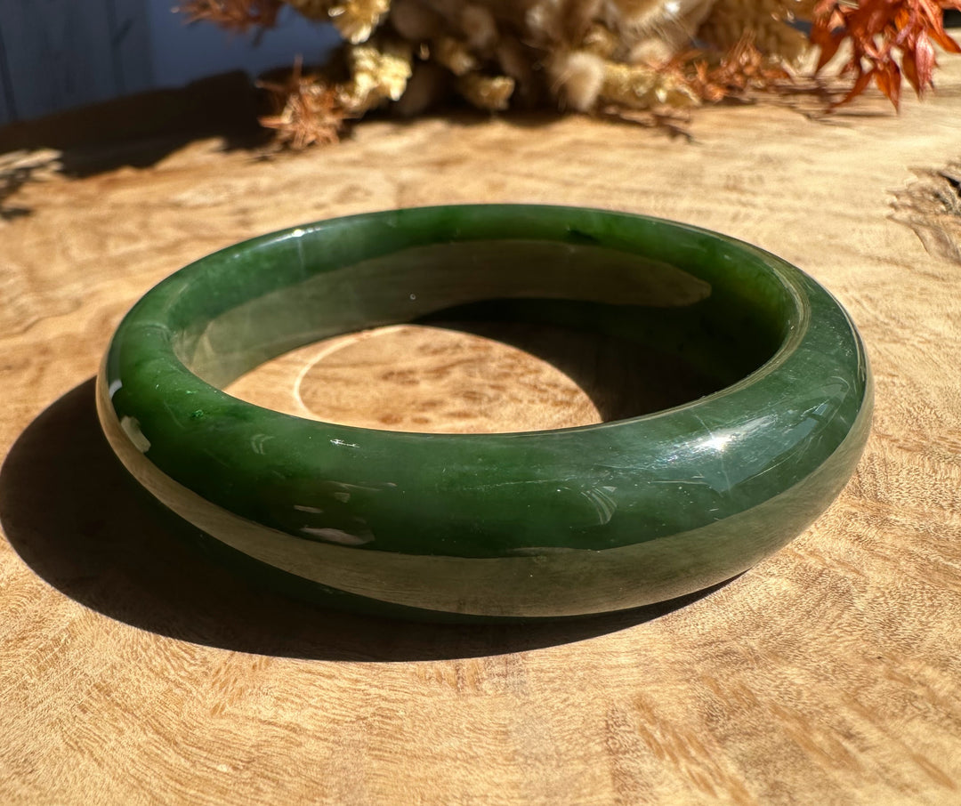 Close up of a polished green jade bangle resting on a wooden surface