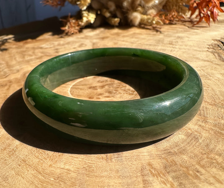Close up of a polished green jade bangle resting on a wooden surface