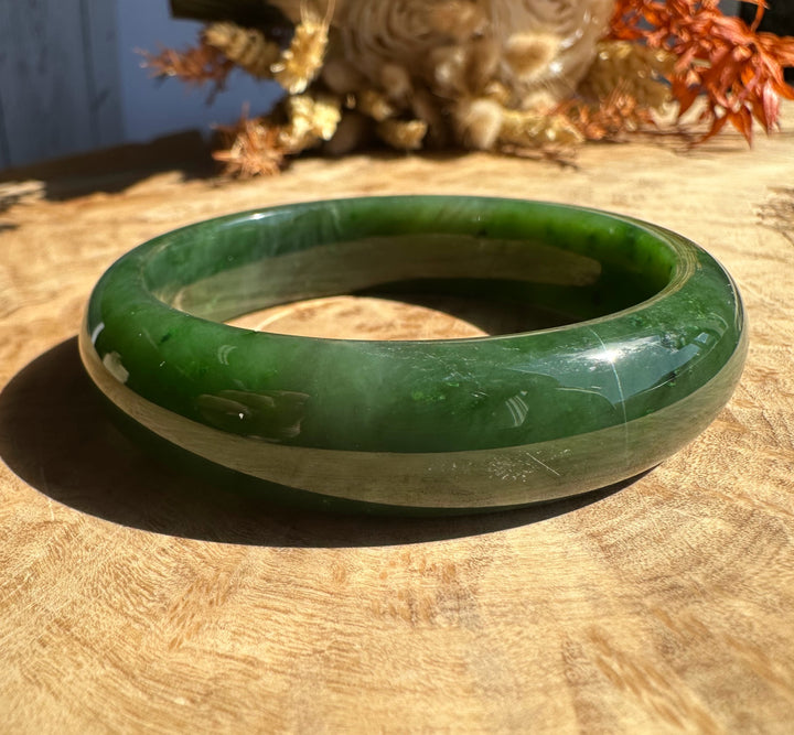Canadian Jade Bangle 56 x 15mm green resting on a sunlit wooden surface.