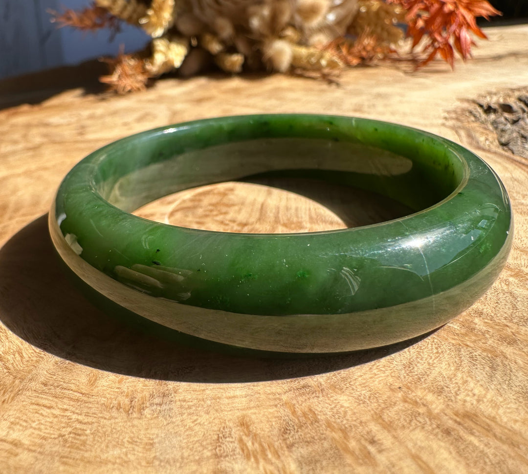 Green jade bangle with a creamy band around its circumference on a wooden surface