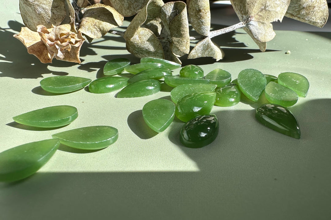 Assorted green nephrite jade pear cabochons scattered on a wooden surface
