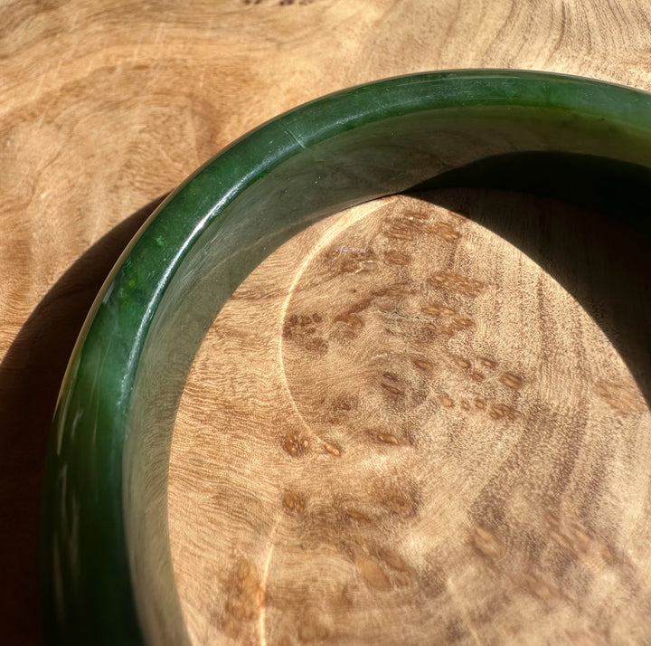 Close-up of Canadian Jade Bangle showing glossy green color and smooth edge on a wooden surface.