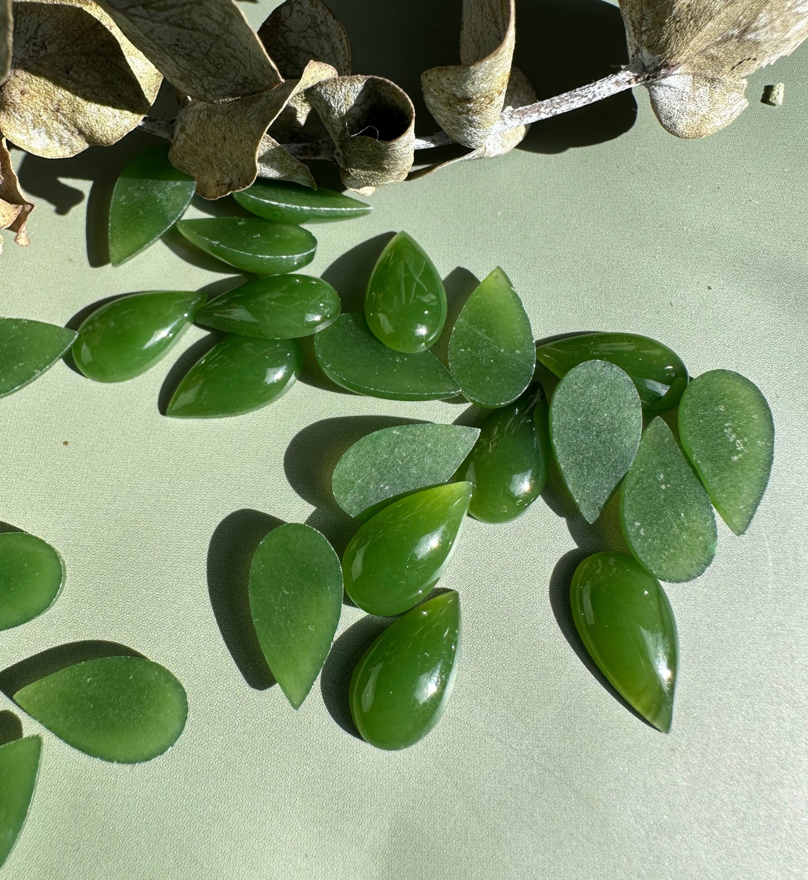 Bright green nephrite jade pear cabochons arranged on a light background.