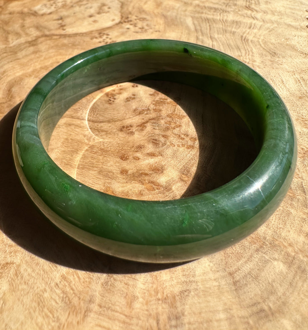 Green jade bangle with a pale stripe around its middle on wood surface