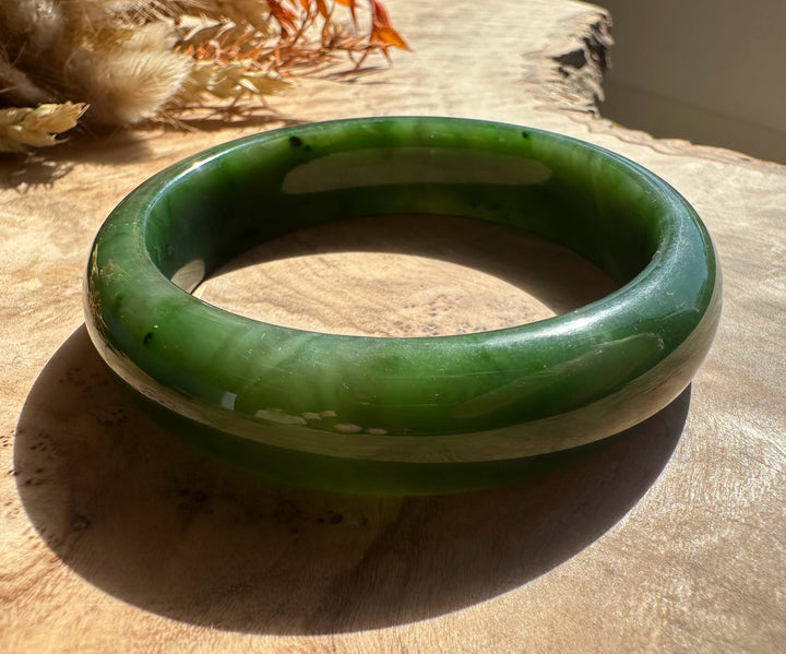 Top view of Canadian Jade Bangle with polished jade surface beside dried flowers on a wooden surface.