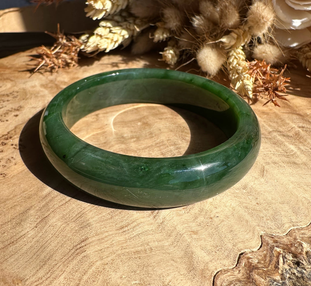 Canadian Jade Bangle 56 x 15mm resting on a wooden surface with dried plant decor