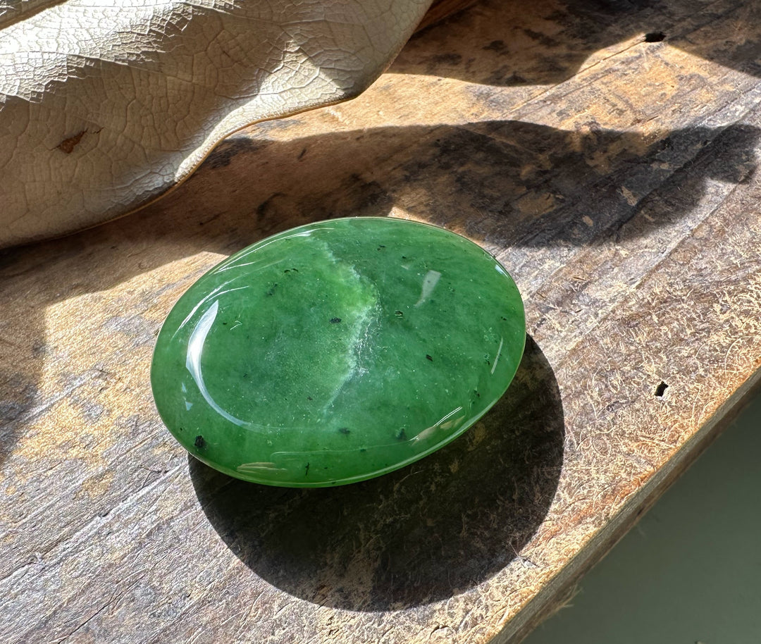 Oval Canadian jade worry stone in bright green resting on a sunlit wooden surface