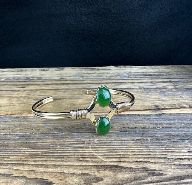 Silver open cuff bracelet with two green jade beads on a rustic wooden surface.