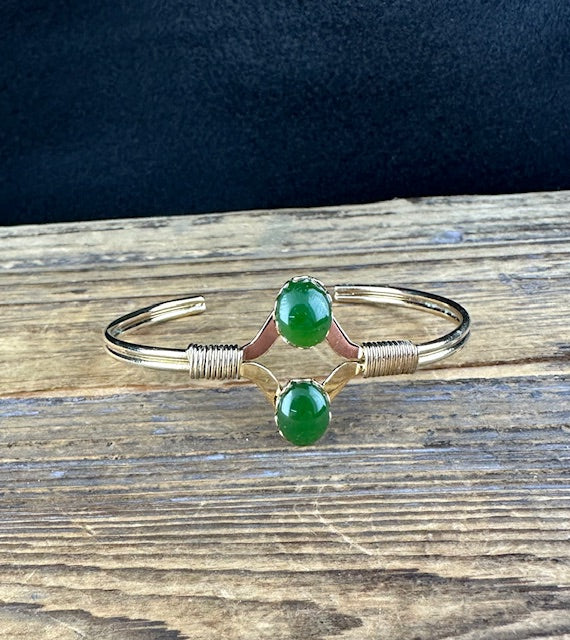 Close-up of vintage jade bracelet with two green beads set in a V-shaped silver frame.