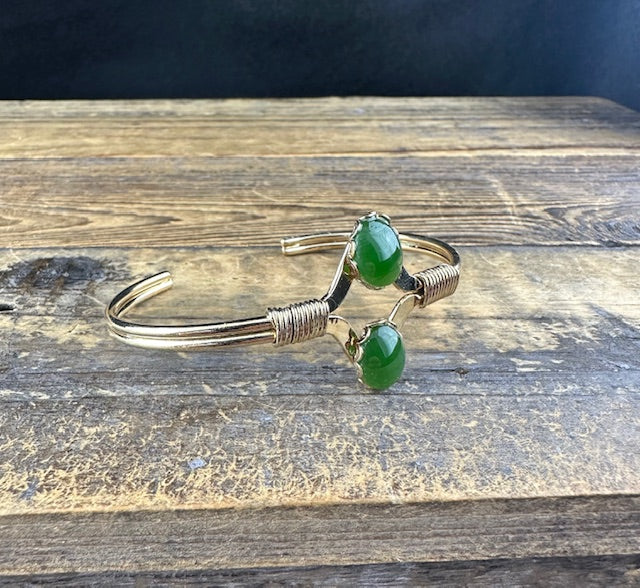 Angle shot of vintage jade bracelet resting on weathered wood showing two green beads.