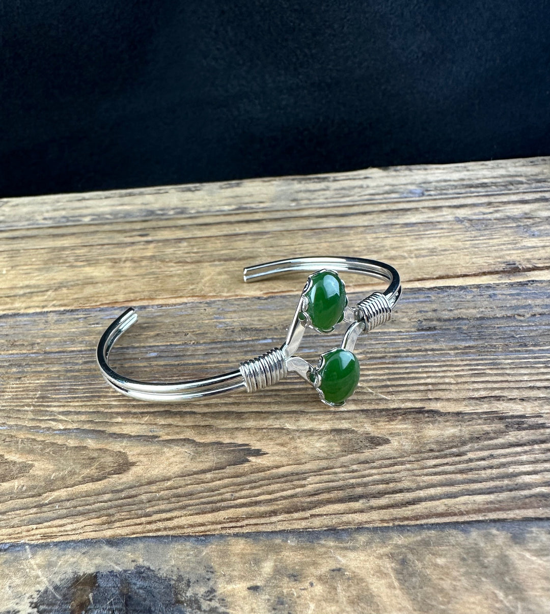 Close up of two green jade stones set on a silver cuff with wrapped coils at the ends.