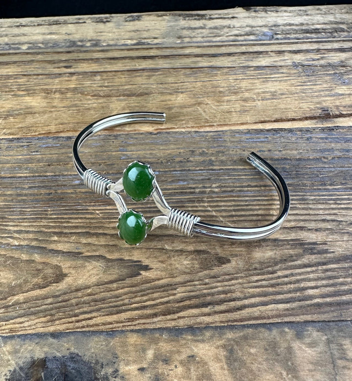 Vintage Jade Bracelet with two green cabochon stones on a silver open cuff resting on wood.