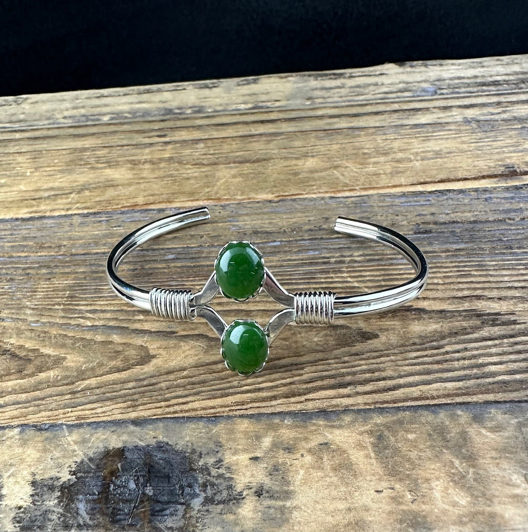 Close-up of Vintage Jade Bracelet showing two green jade beads set in a decorative silver frame on a polished cuff.