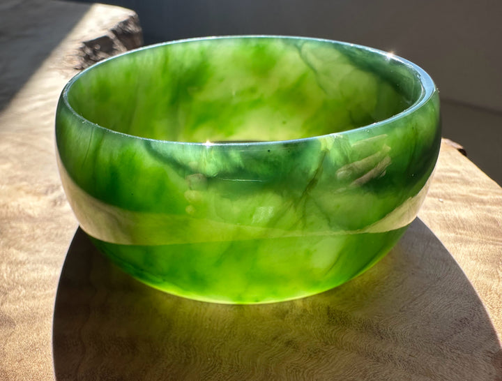 A Grade Ogden jade bangle in bright green marbled tones resting on a wooden surface