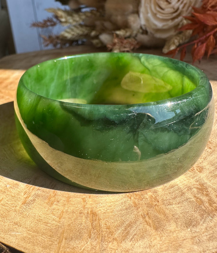 Close-up of a green Ogden jade bangle with lighter banding resting on a wooden surface.