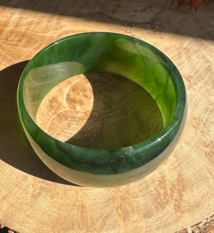 A Grade Ogden Jade Bangle resting on a wooden surface showing a thick rounded green jade ring