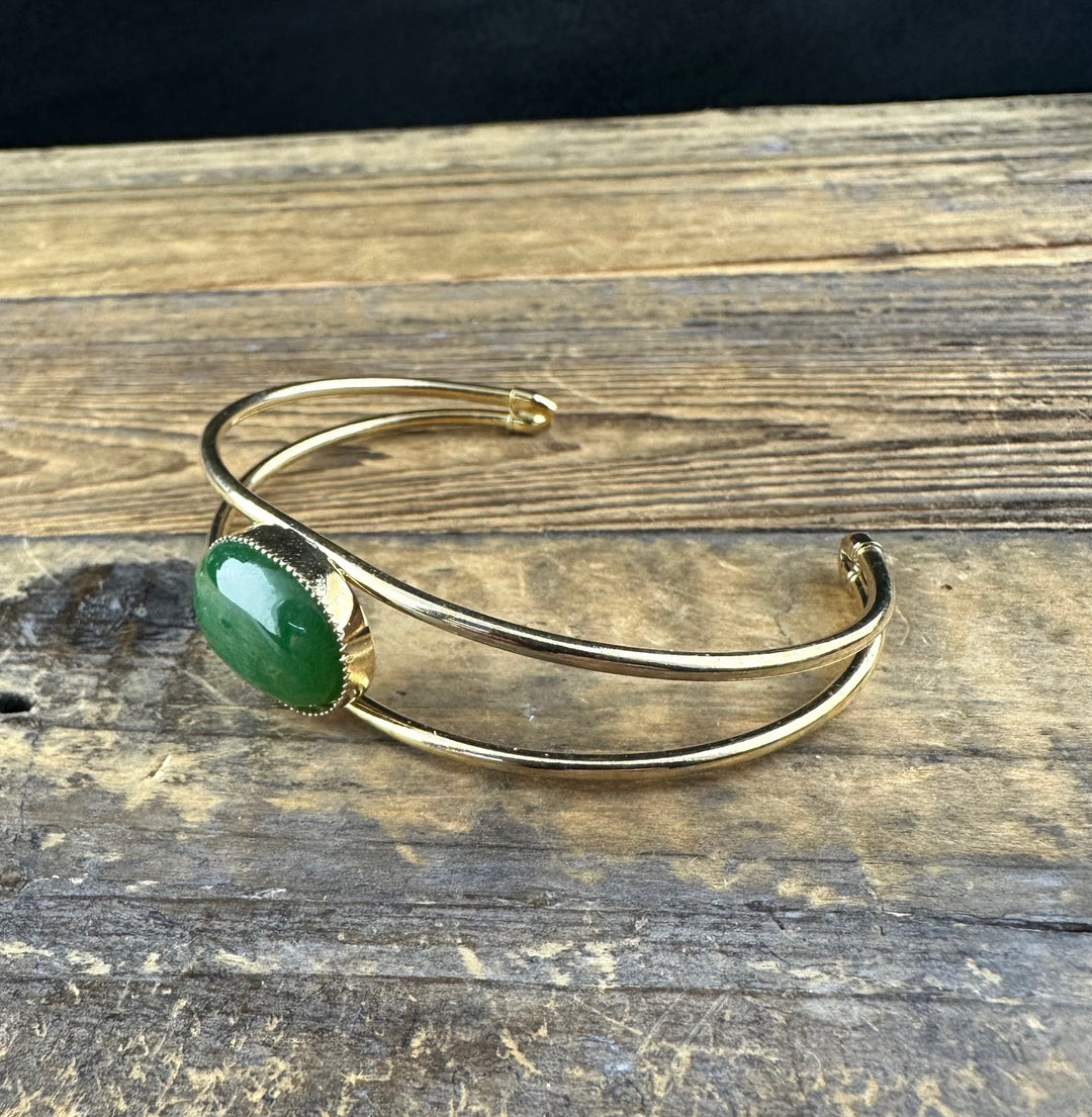 Gold cuff bracelet with a green jade cabochon in a beaded bezel, shown from the side