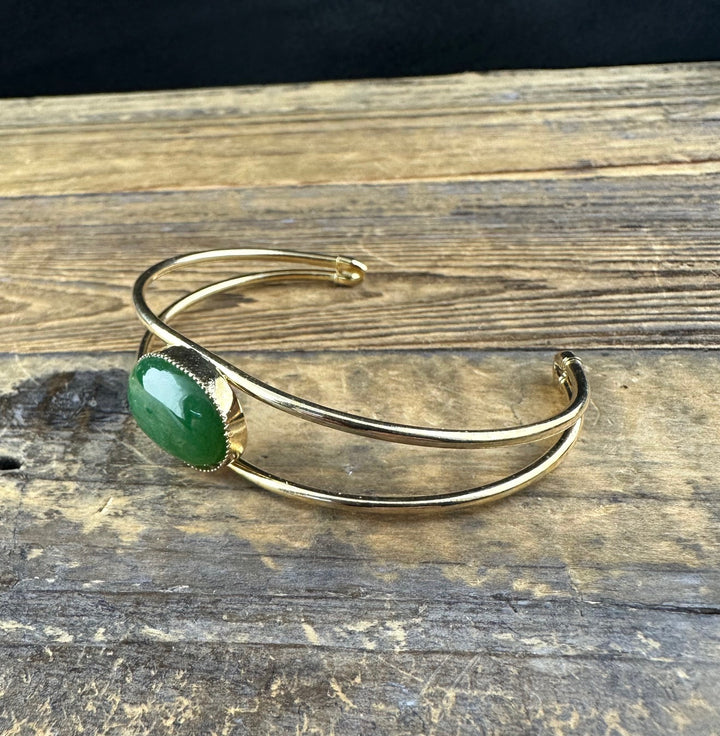Gold cuff bracelet with a green jade cabochon in a beaded bezel, shown from the side