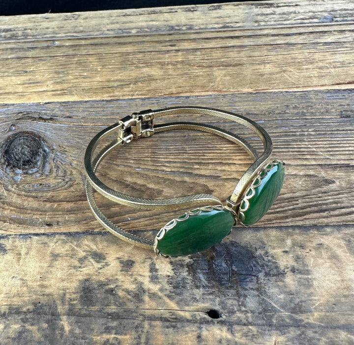 Vintage jade bracelet with two green jade cabochons set in gold frames on a textured gold band displayed on wood