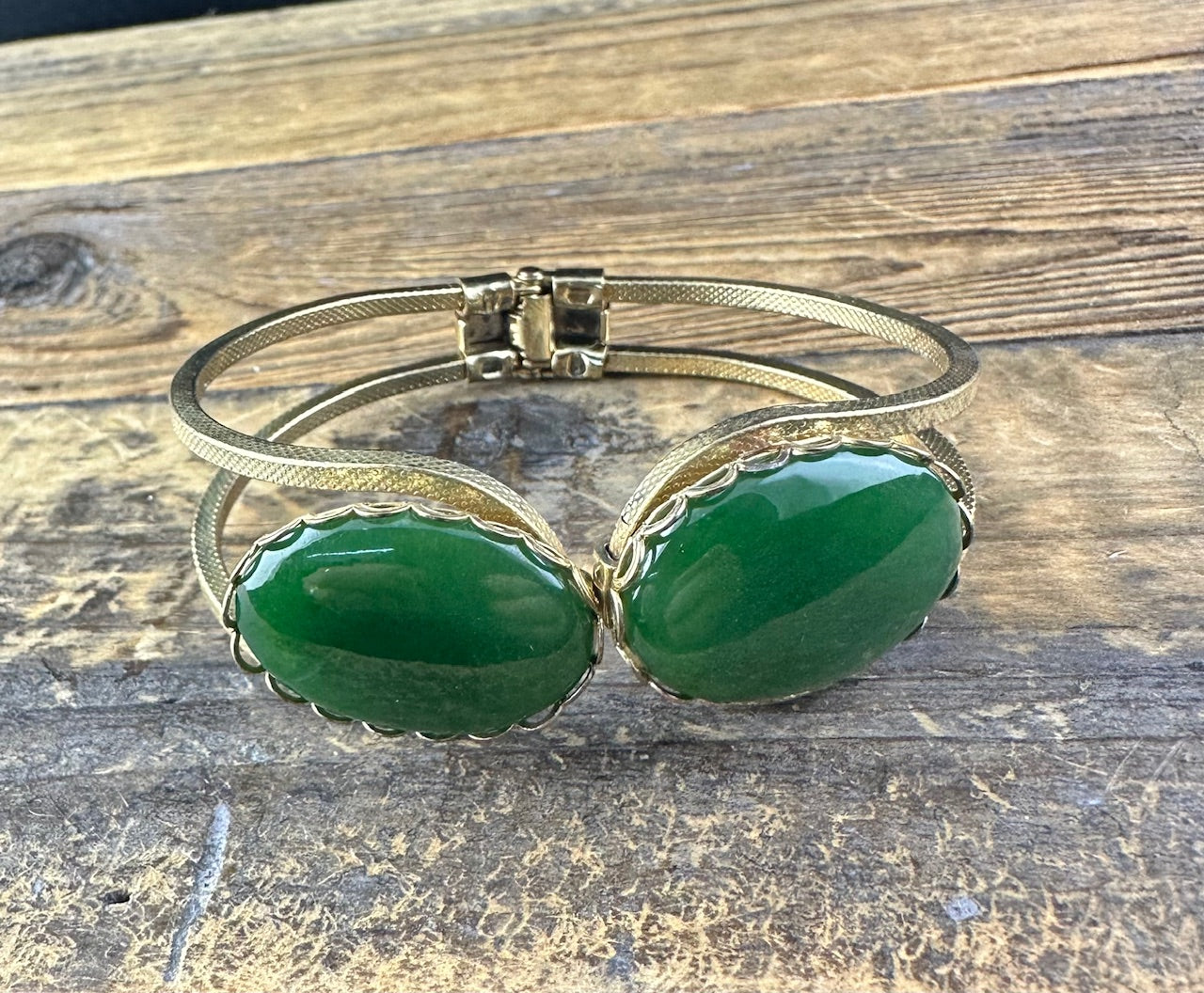Two oval green jade cabochons in scalloped gold bezels on a textured gold bracelet.