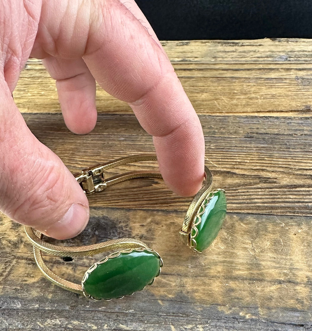 Hand holds the vintage jade bracelet showing the gold mesh band and green oval jade centerpiece from the side.