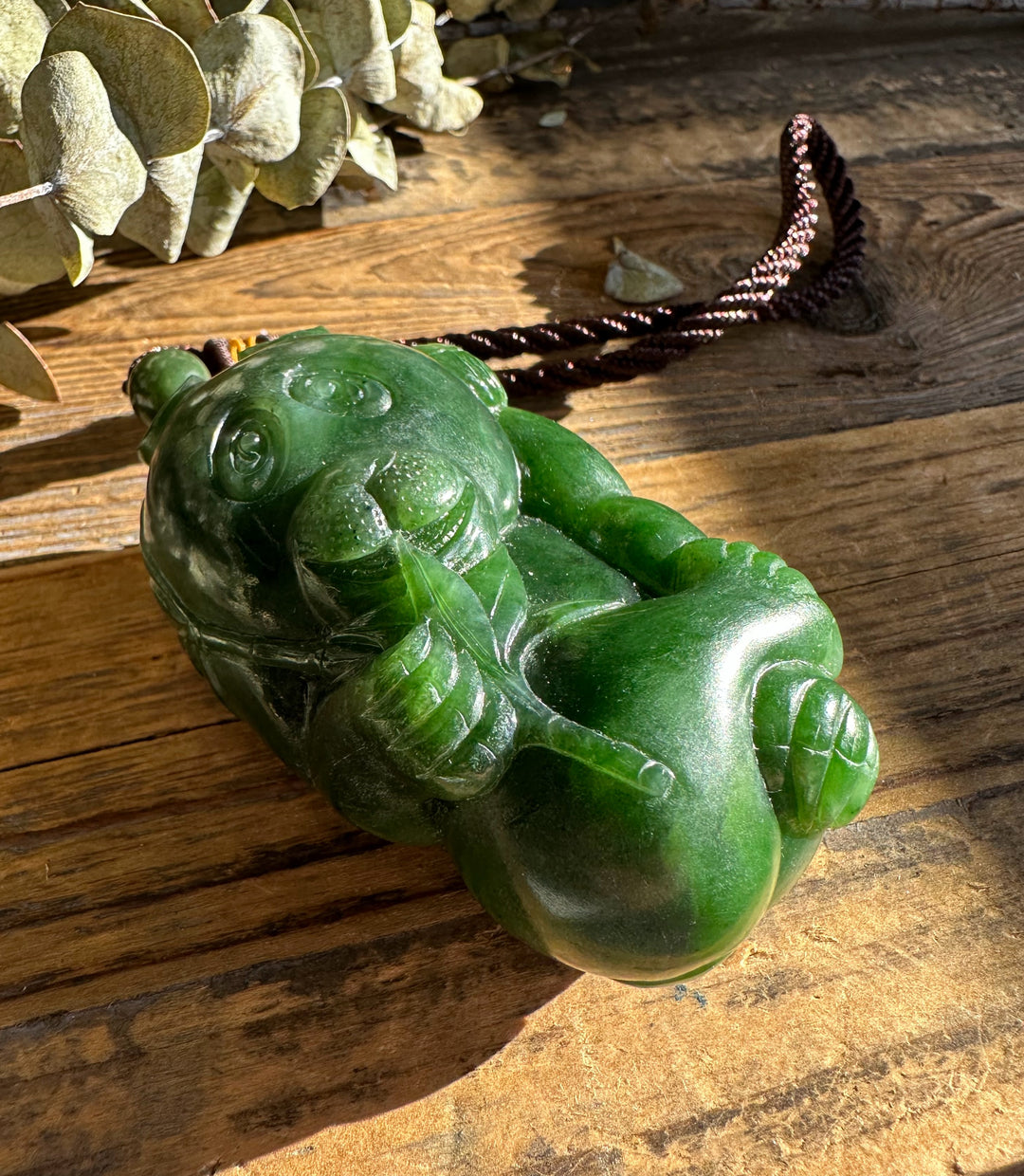Green jade Panda Pocket Pendant resting on wood with the cord extended to the right