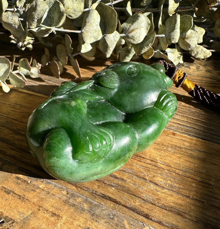 Close up of green jade Panda Pocket Pendant showing carved limbs with braided cord on a wooden surface