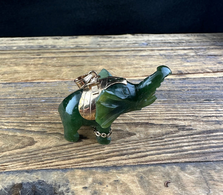 Vintage jade elephant pendant resting on a green jade elephant statue with a gold bail