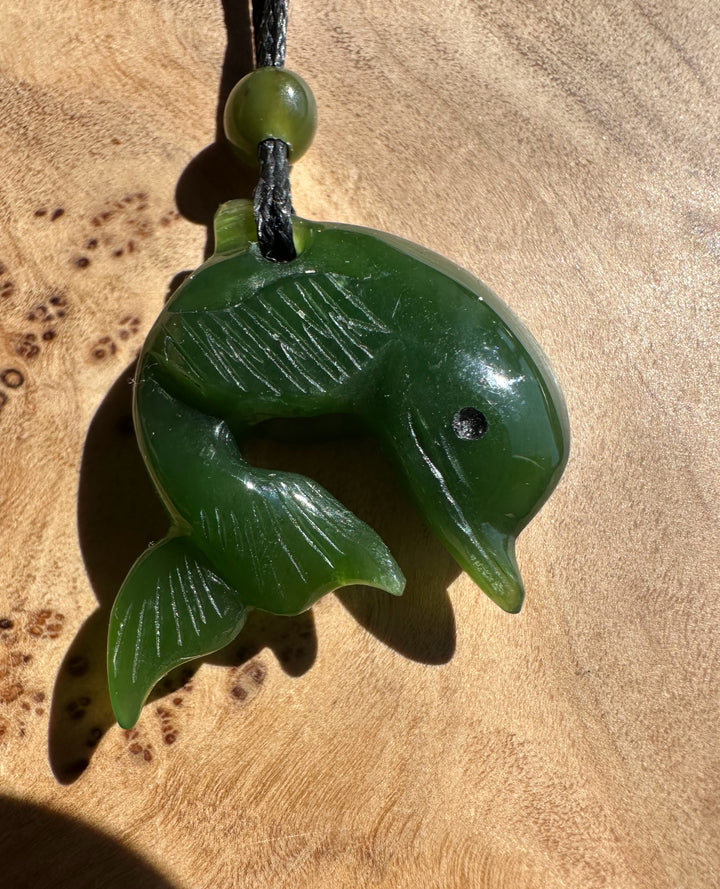 AA Cassiar jade dolphin pendant in green with black cord and bead.