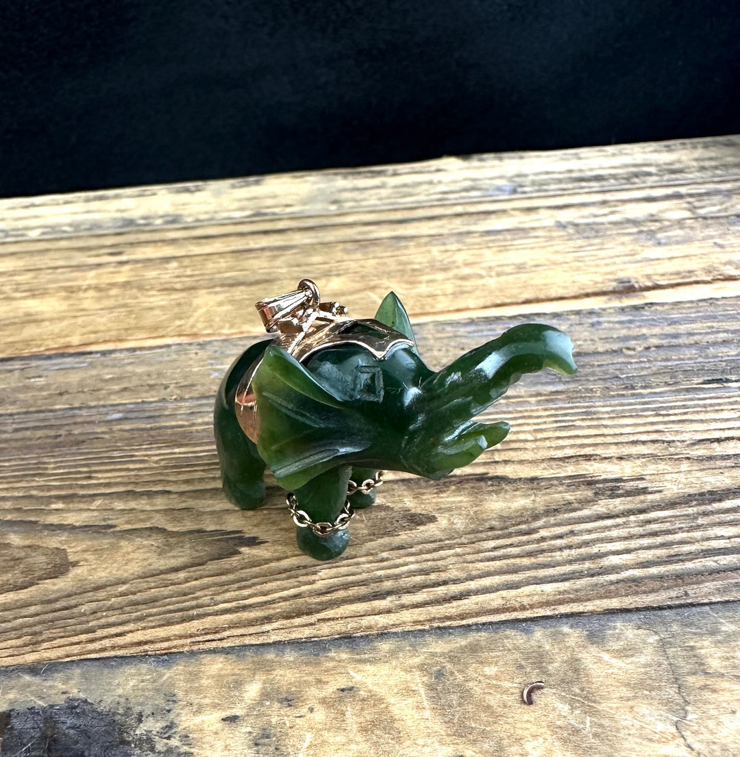 Jade elephant pendant on black cord with gold bail shown on weathered wood with a coin for scale
