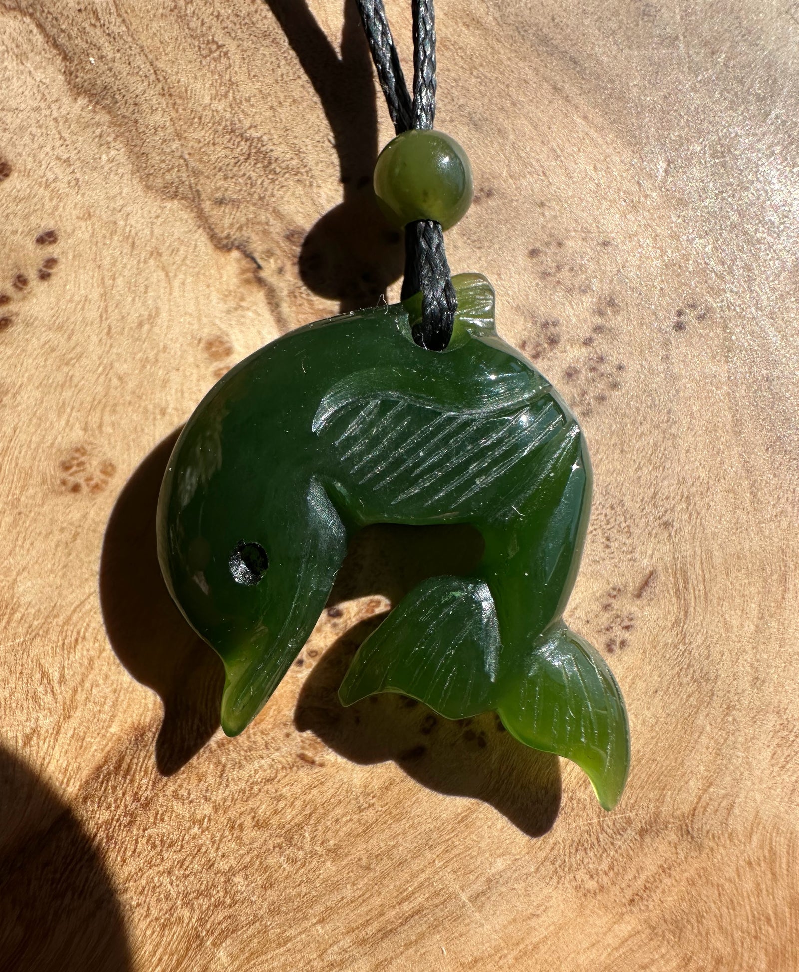 Deep green jade dolphin pendant hanging from a black cord with a green bead near the top