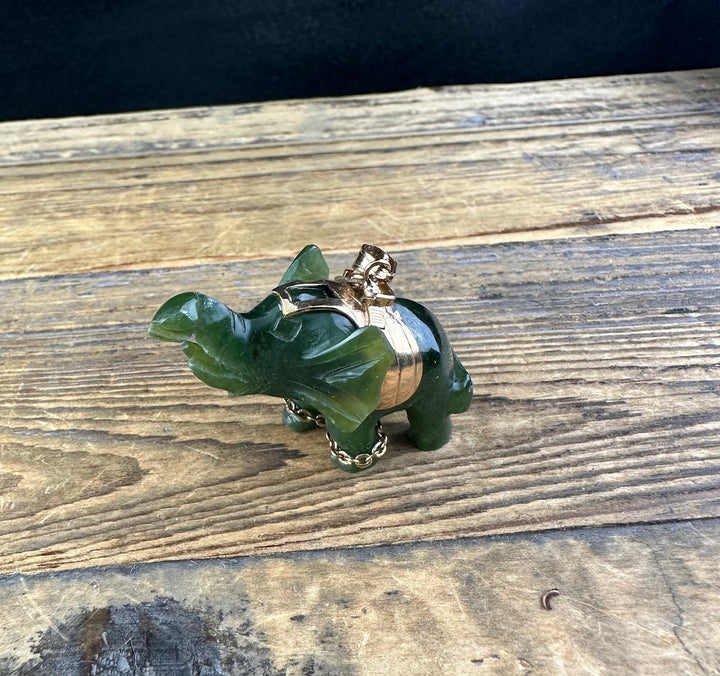 Vintage jade elephant pendant with gold saddle and chain on rustic wood surface